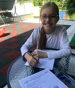 Усмихната ученичка пише домашна работа на открито